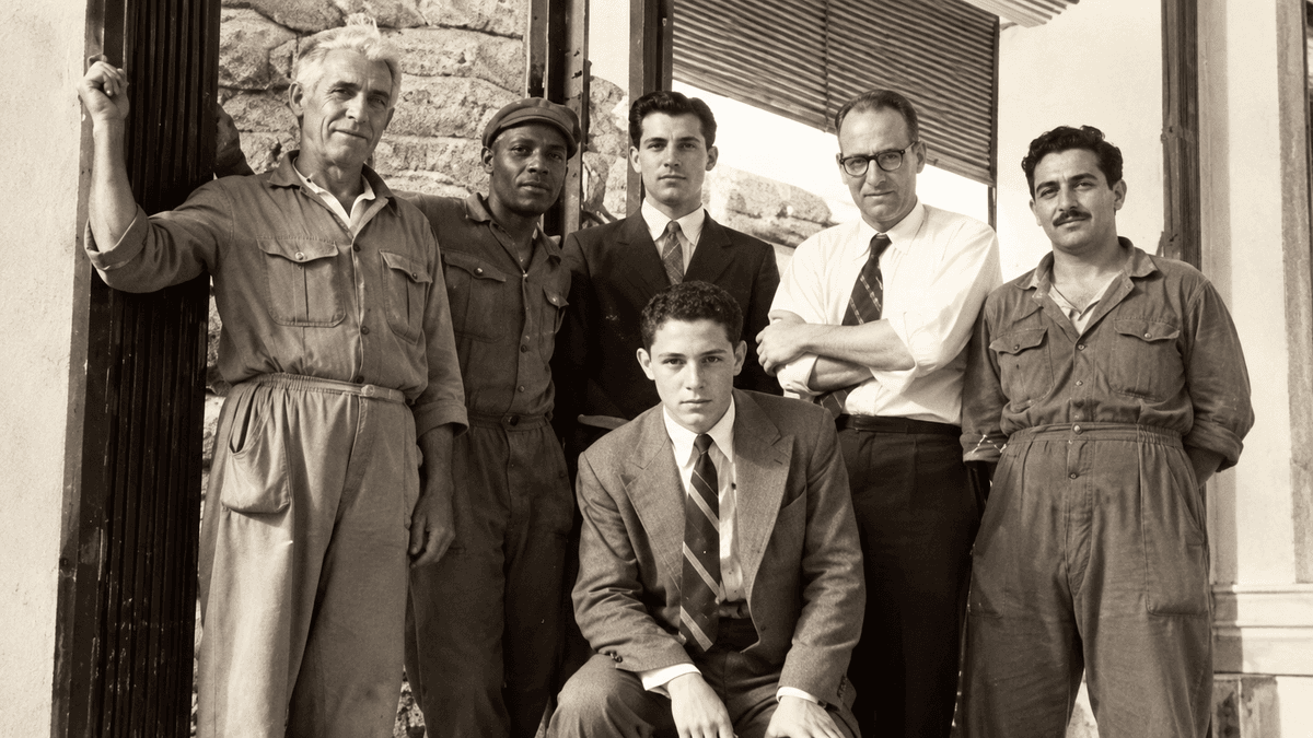 Ilustração de operários e técnicos reunidos diante de uma fábrica nos anos 1950, década em que a Suzano passou a produzir celulose de eucalipto. Imagem gerada por inteligência artificial, sem valor documental